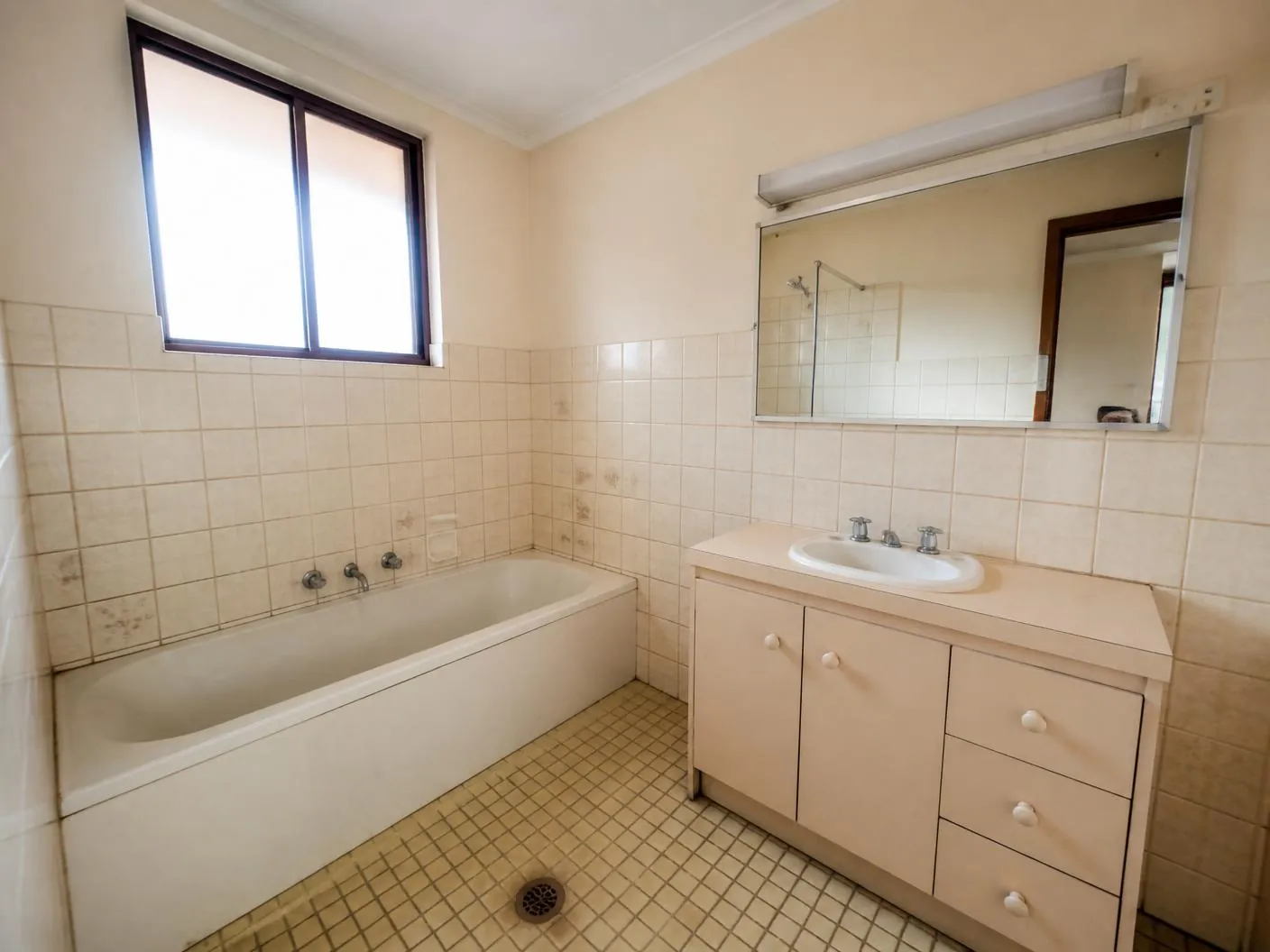 Dated ensuite before renovation with cream tiles, old bath and laminate vanity