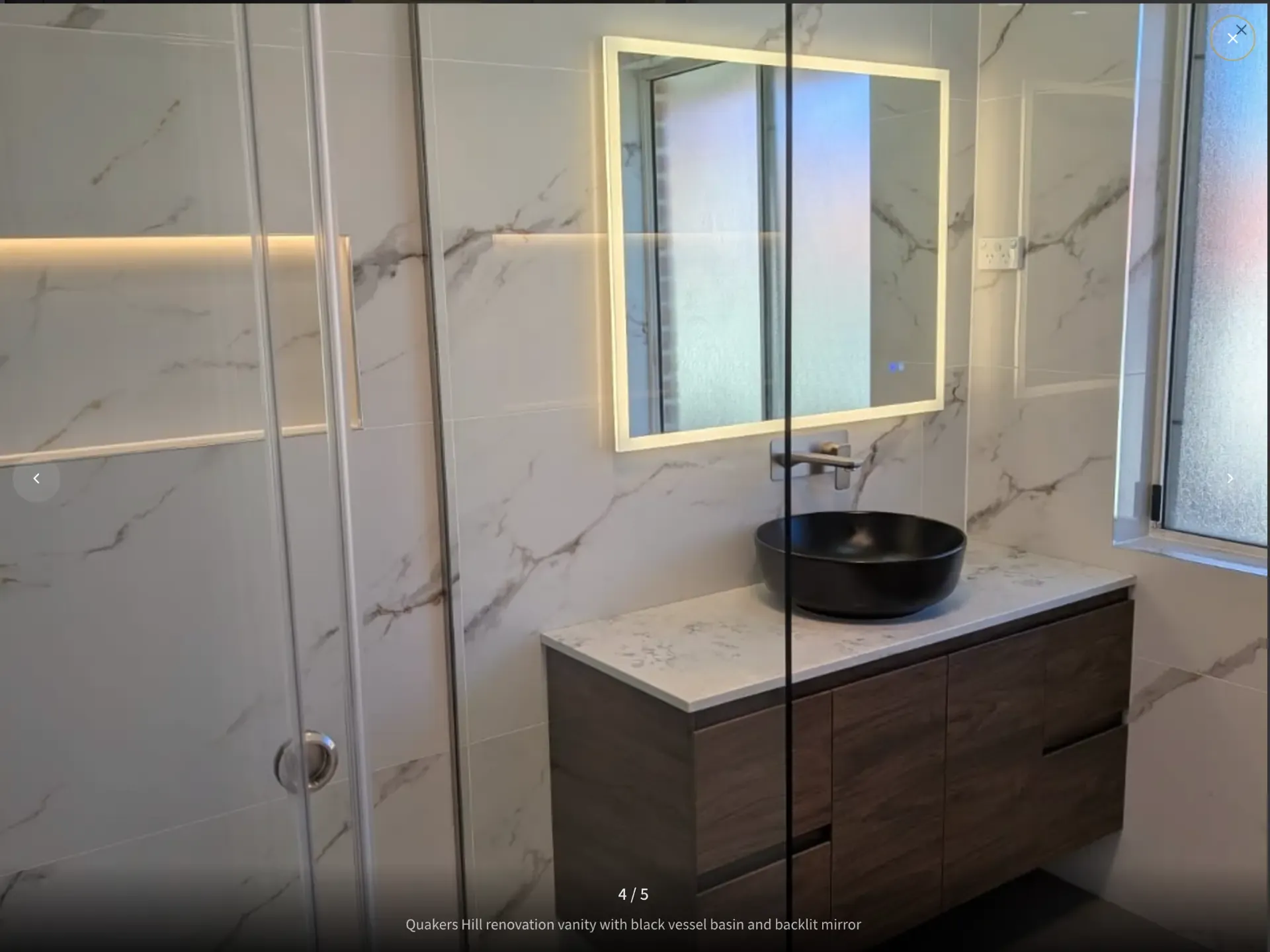 Quakers Hill bathroom after renovation with marble-look walls, timber vanity, black vessel basin and backlit mirror